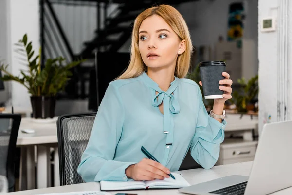 Porträt einer Geschäftsfrau mit Coffee to go am Arbeitsplatz mit Laptop und Notizbuch — Stockfoto