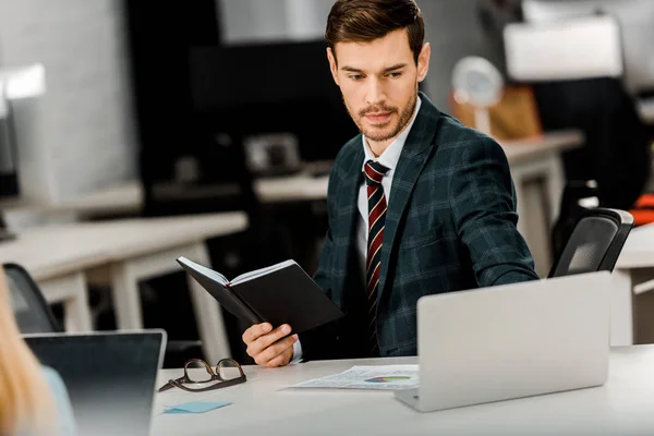 Focused businessman with notebook working on laptop in office — Stock Photo