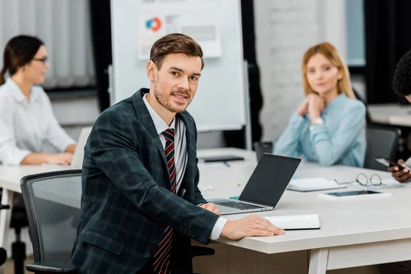 Selective focus of young businessman in suit and multiracial colleagues in office — Stock Photo