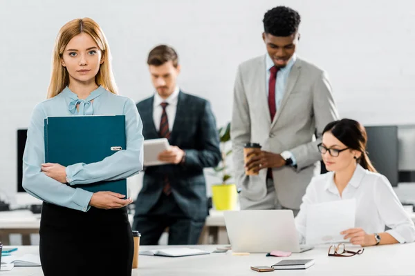 Selective focus of businesswoman with folder and multiethnic colleagues in office — Stock Photo