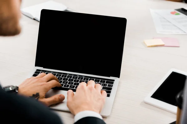 Partial view of businessman typing on laptop with blank screen in office — Stock Photo