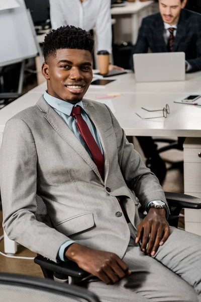 Sonriente hombre de negocios afroamericano mirando la cámara en el lugar de trabajo en la oficina - foto de stock