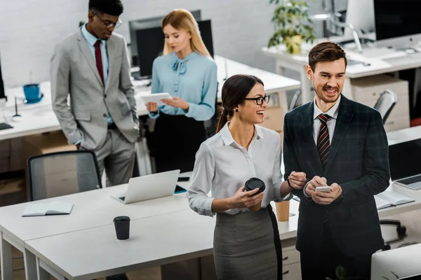 Vue grand angle des hommes d'affaires multiraciaux avec café à emporter et smartphone au bureau — Photo de stock