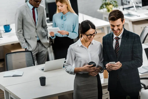 Vue grand angle des hommes d'affaires multiraciaux avec café à emporter et smartphone au bureau — Photo de stock