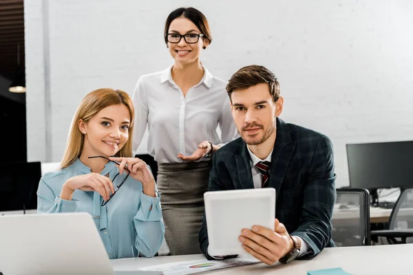 Portrait of businessman with tablet and businesswomen at workplace with laptop in office — Stock Photo