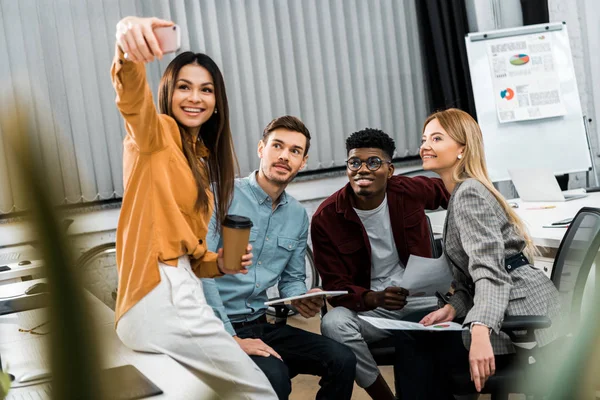 Empresários multiculturais sorridentes levando selfie no smartphone durante o trabalho no escritório — Fotografia de Stock