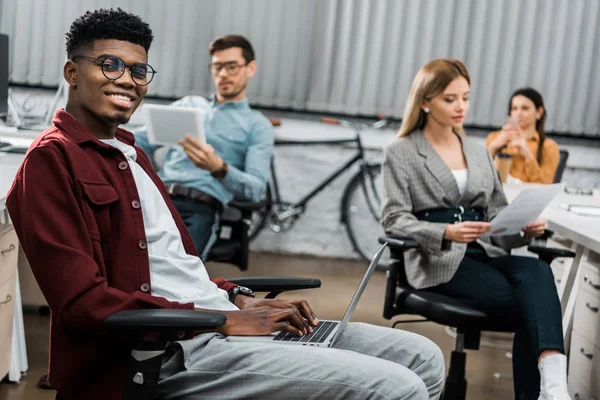 Jovens empresários multiculturais com papéis e dispositivos digitais no escritório — Fotografia de Stock