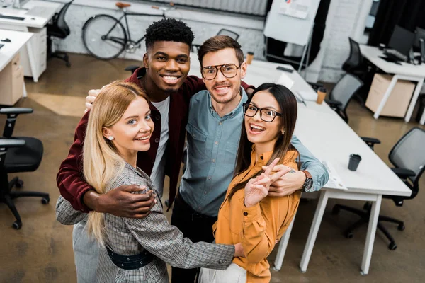 Hochwinkelaufnahme multiethnisch zufriedener Geschäftskollegen, die im Büro in die Kamera schauen — Stockfoto