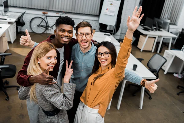 Hochwinkelaufnahme multiethnisch zufriedener Geschäftskollegen, die im Büro in die Kamera schauen — Stockfoto