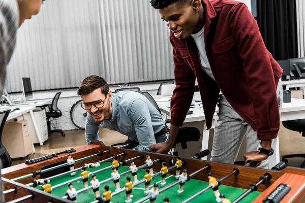 Des hommes d'affaires multiculturels souriants jouant au baby-foot au bureau — Photo de stock