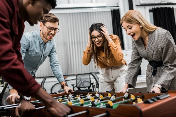 Emotivi colleghi d'affari multiculturali che giocano a calcio balilla insieme in ufficio — Foto stock