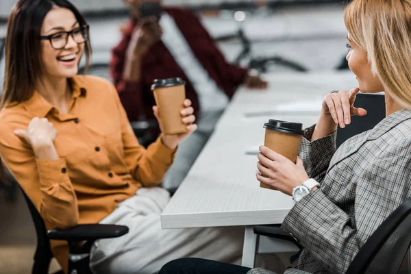 Smiling young businesswomen with coffee to go at workplace in office — Stock Photo