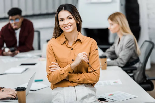 Smiling businesswoman looking at camera with multicultural colleagues behind in office — Stock Photo