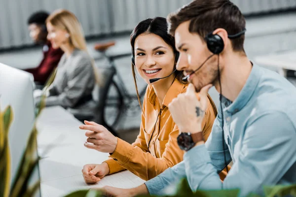 Foco seletivo de operadores de call center sorridentes e colegas multiétnicos no escritório — Fotografia de Stock