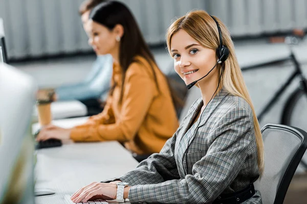 Selektiver Fokus eines lächelnden Callcenter-Betreibers, der im Büro in die Kamera blickt — Stockfoto