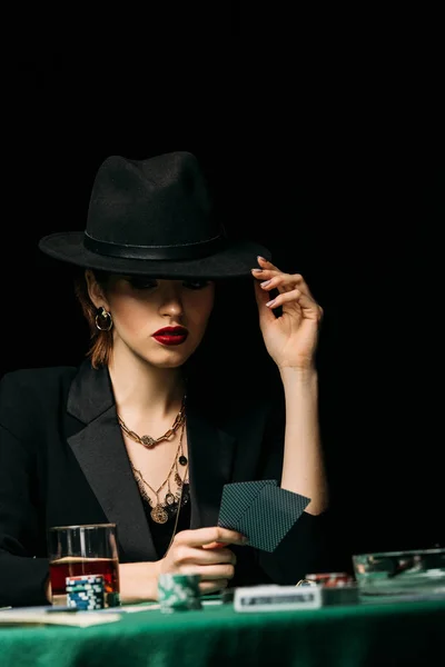 Surface level of attractive girl in jacket touching hat playing poker in casino — Stock Photo