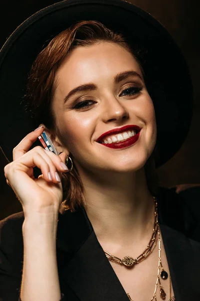 Menina atraente feliz em casaco e chapéu segurando fichas de poker e olhando para a câmera — Fotografia de Stock