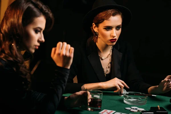 Jolies filles en vêtements noirs jouant au poker à table dans le casino — Photo de stock