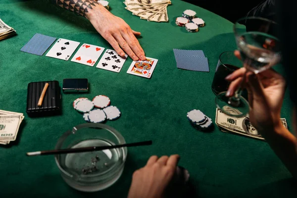 Imagen recortada de la mujer y el hombre tatuado jugando mesa de póquer en el casino, niña sosteniendo vaso de cóctel - foto de stock