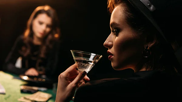 Chica atractiva beber cóctel mientras juega al póquer en la mesa en el casino - foto de stock