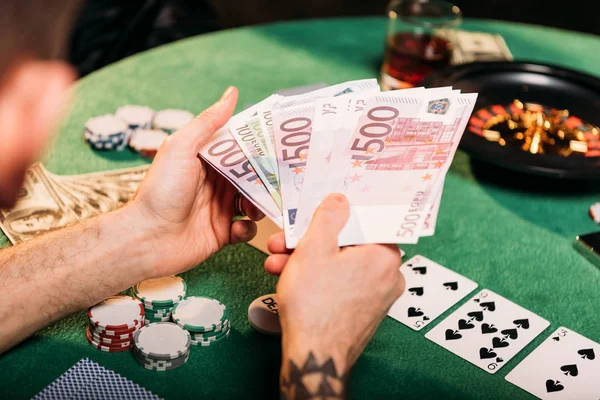Imagen recortada del hombre tatuado sosteniendo billetes en euros en la mesa de póquer en el casino - foto de stock