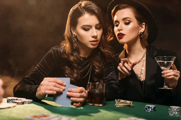 Jolies filles jouant au poker à table dans le casino, femme pointant sur quelque chose à un ami — Photo de stock