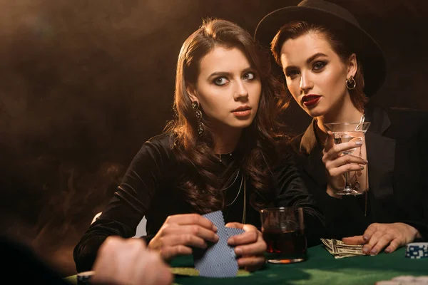Hermosas mujeres jugando al póquer en la mesa en el casino y mirando hacia otro lado - foto de stock