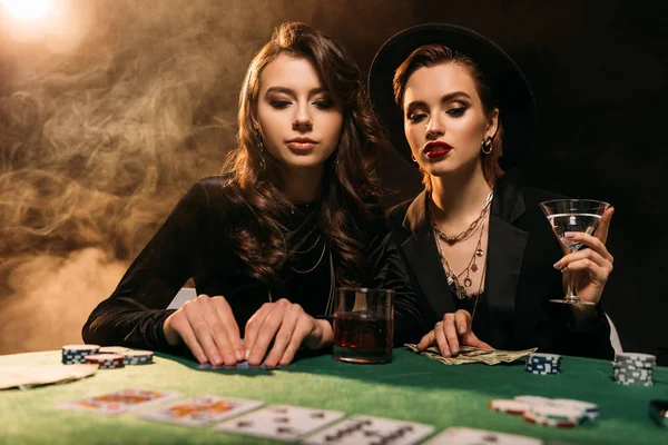 Attractive girls in black clothes playing poker at table in casino — Stock Photo