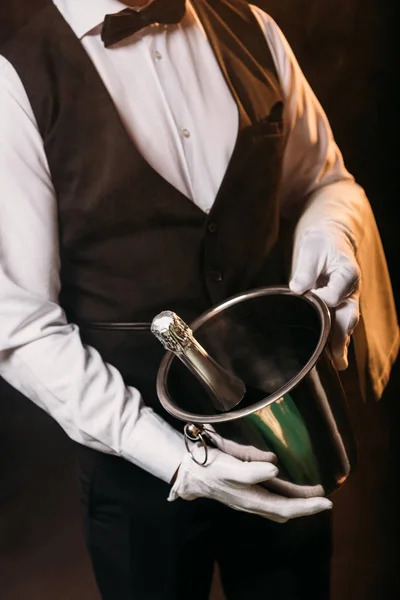 Cropped image of waiter holding bottle of champagne in bucket on black — Stock Photo