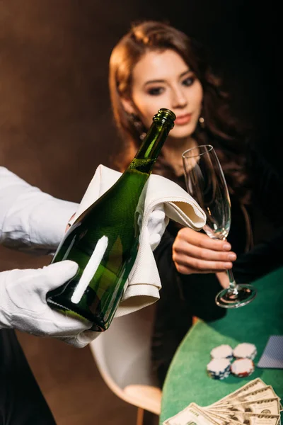 Selective focus of waiter pouring champagne in glass for attractive girl at poker table in casino — Stock Photo