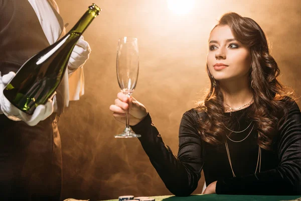 Waiter pouring champagne in glass for beautiful girl at poker table in casino — Stock Photo