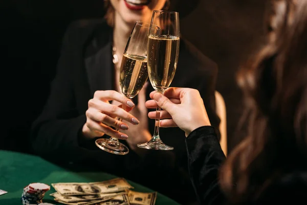 Imagen recortada de las niñas felices tintineo con copas de champán en la mesa de póquer en el casino - foto de stock