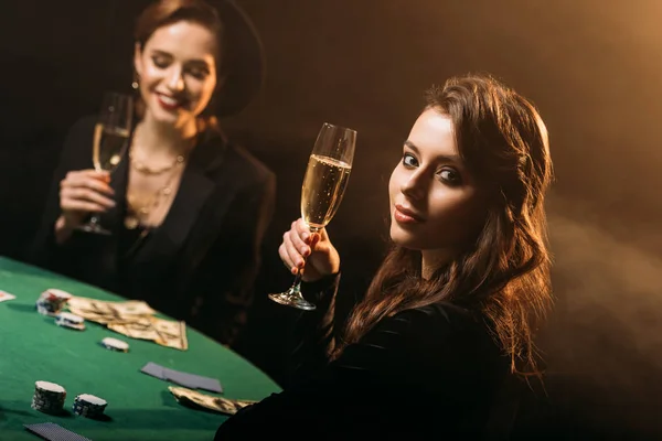 Meninas atraentes segurando copos de champanhe na mesa de poker no cassino — Fotografia de Stock