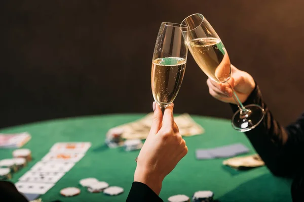 Imagen recortada de las mujeres tintineo con copas de champán en la mesa de póquer en el casino - foto de stock