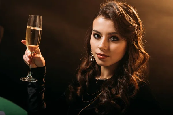 Chica atractiva sosteniendo la copa de champán y mirando a la cámara en marrón - foto de stock