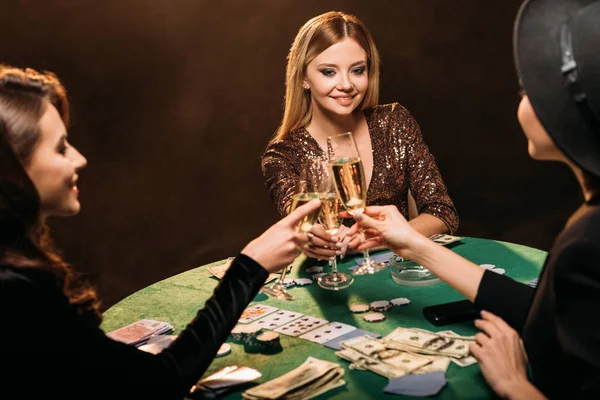 Chicas atractivas feliz tintineo con copas de champán en la mesa de póquer en el casino - foto de stock