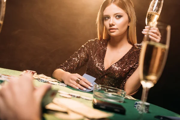 Menina atraente segurando copo de champanhe na mesa de poker no casino e olhando para longe — Fotografia de Stock