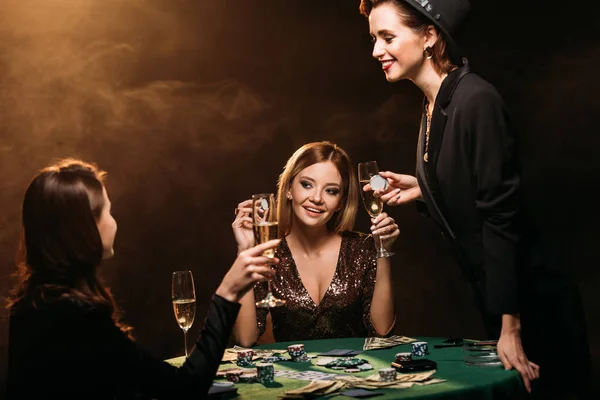 Happy beautiful women with glasses of champagne talking at poker table in casino — Stock Photo