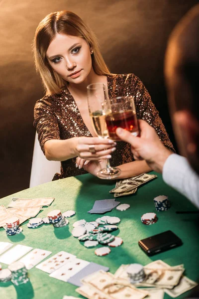Chica atractiva y croupier tintineo con vasos de bebidas alcohólicas mientras juega al póquer en el casino - foto de stock
