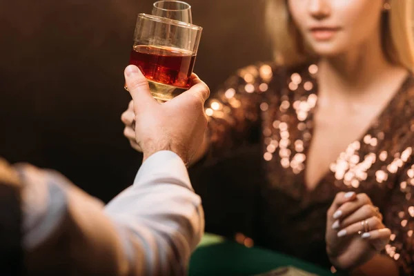 Imagen recortada de chica y croupier tintineo con vasos de bebidas alcohólicas mientras juega al póquer en el casino - foto de stock