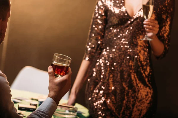 Immagine ritagliata di ragazza e croupier che tiene bicchieri di bevande alcoliche al tavolo da poker nel casinò — Foto stock