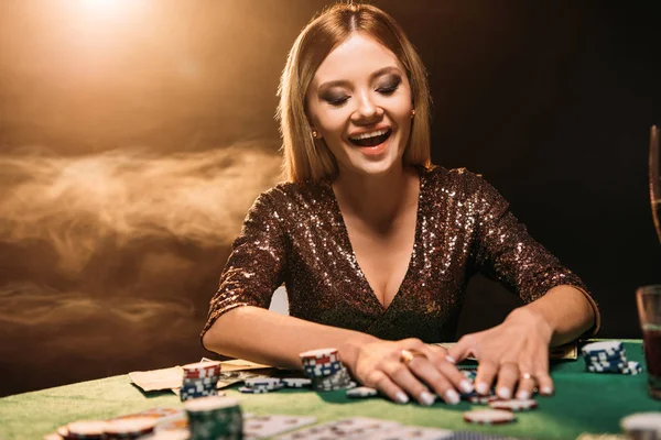 Счастливая привлекательная девушка берет фишки для покера и смотрит вниз на казино — стоковое фото