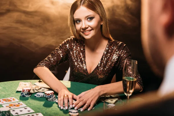 Foco seletivo de sorrir menina atraente tomando fichas de poker e olhando para croupier no cassino — Fotografia de Stock