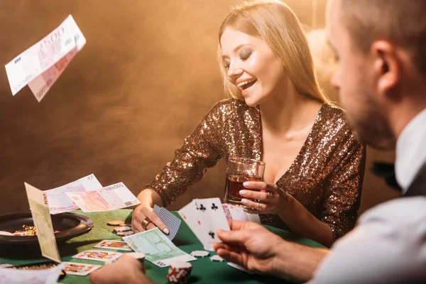Chica atractiva feliz jugando al póquer con croupier en el casino, billetes en euros que caen en la mesa - foto de stock