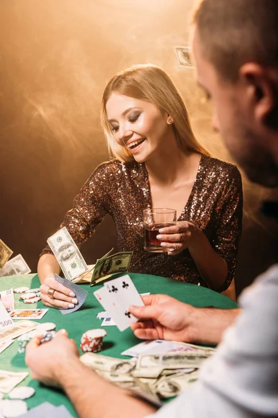 Feliz hermosa chica jugando al póquer con croupier en el casino, billetes de dólar cayendo en la mesa - foto de stock