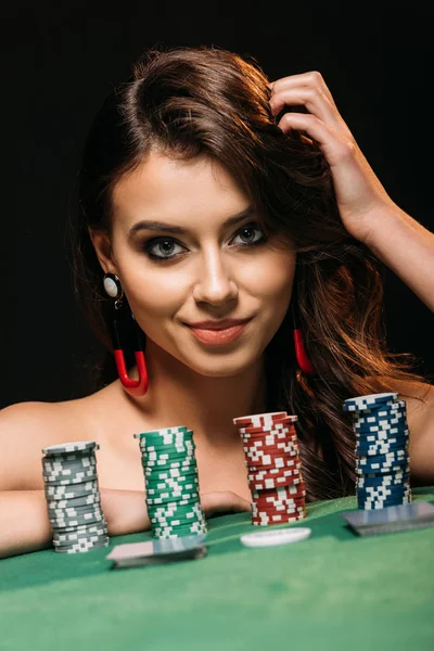 Menina atraente inclinando-se na mesa com fichas de poker e olhando para a câmera isolada no preto — Fotografia de Stock