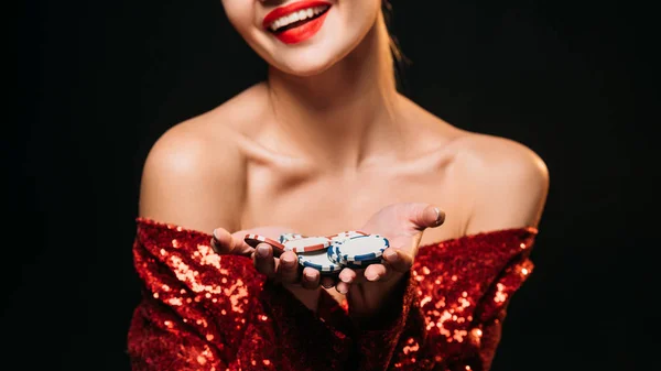 Imagen recortada de la chica sonriente en vestido brillante rojo con fichas de casino aislados en negro - foto de stock