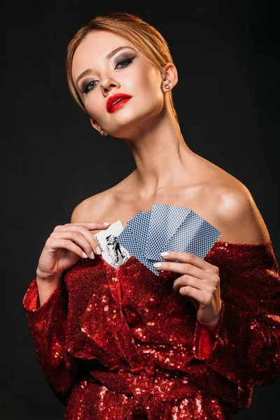 Atractiva chica en rojo brillante vestido esconder tarjeta joker en vestido aislado en negro - foto de stock