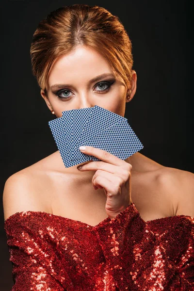 Attraktives Mädchen in rotem, glänzendem Kleid, das sich von Spielkarten isoliert auf schwarz abhebt — Stockfoto