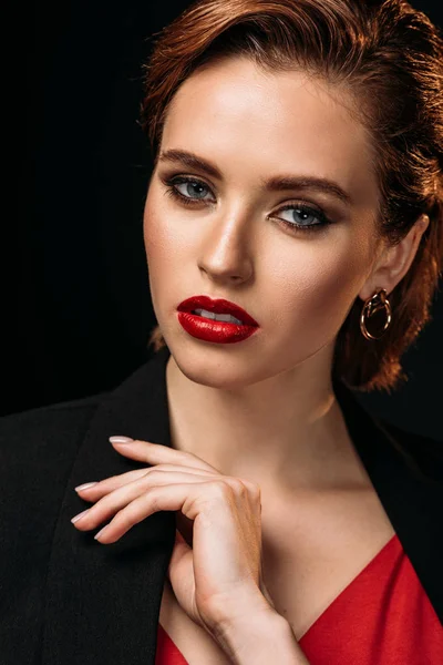 Portrait of beautiful woman in red dress and black jacket looking at camera isolated on black — Stock Photo